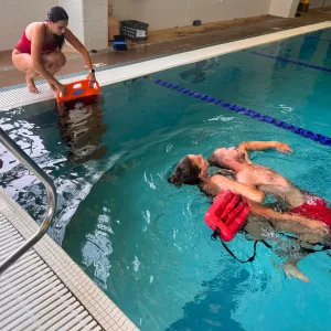 3 lifeguards doing a training exercise in the pool.