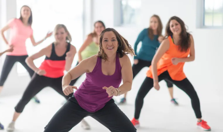 A group of women smiling and moving in a group exercise class. 