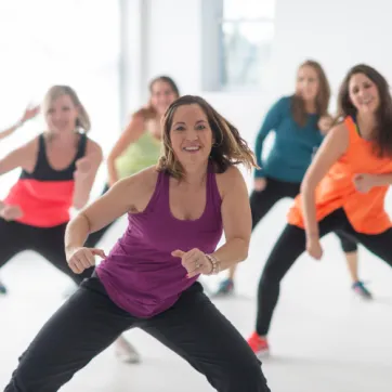 A group of women smiling and moving in a group exercise class. 